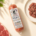 A tube of Birmingham Raw Beef raw dog food, shown on a light beige surface next to raw meat