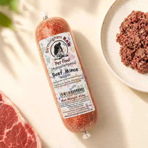 A tube of Birmingham Raw Beef raw dog food, shown on a light beige surface next to raw meat