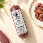 A tube of Birmingham Raw Duck raw dog food, shown on a light beige surface next to raw meat