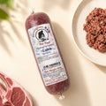 A tube of Birmingham Raw Lamb raw dog food, shown on a light beige surface next to raw meat