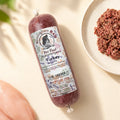 A packaged tube of Birmingham Raw pet food, labeled 'Turkey', in a flat-lay with raw turkey fillet on a light cream background.