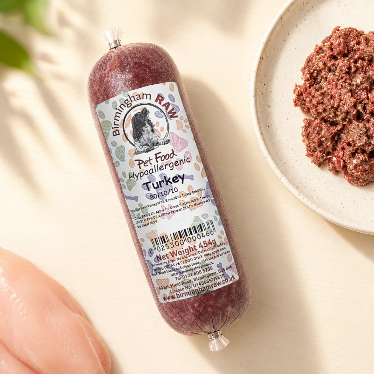 A packaged tube of Birmingham Raw pet food, labeled 'Turkey', in a flat-lay with raw turkey fillet on a light cream background.