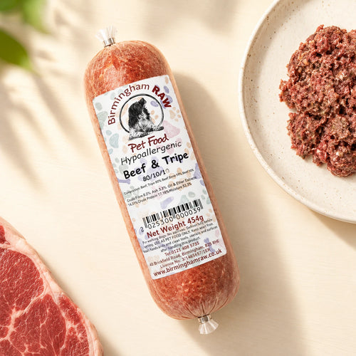 A tube of Birmingham Raw Beef And Tripe raw dog food, shown on a light beige surface next to raw meat