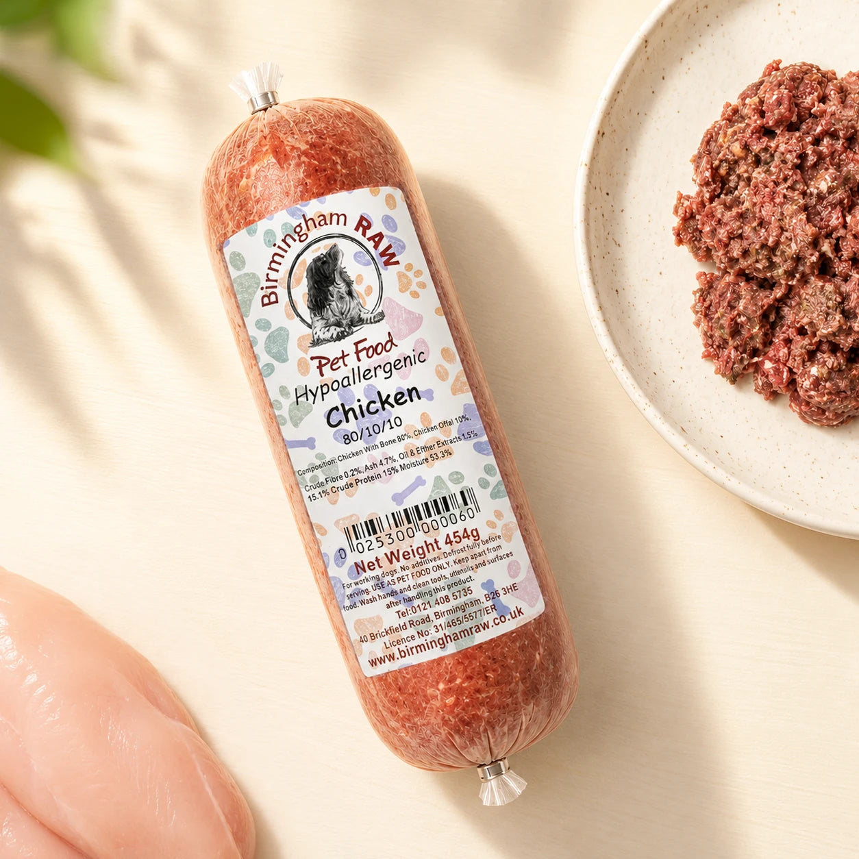 A tube of Birmingham Raw chicken raw dog food, shown on a light beige surface next to raw meat
