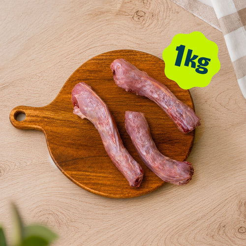 A pile of Birmingham Raw duck neck dog treats sold by the kilogram, displayed on a round wooden cutting board over a light wood kitchen unit.