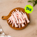 A pile of Birmingham Raw chicken feet dog treats sold by the kilogram, displayed on a round wooden cutting board over a light wood kitchen unit.
