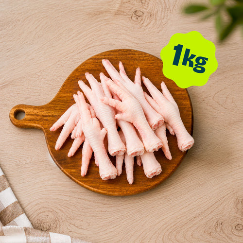 A pile of Birmingham Raw chicken feet dog treats sold by the kilogram, displayed on a round wooden cutting board over a light wood kitchen unit.