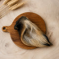 A hair cow ear dog treat, displayed on a round wooden cutting board over a light wood kitchen unit.