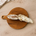 A hair rabbit ear dog treat, displayed on a round wooden cutting board over a light wood kitchen unit.