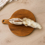 A hair rabbit ear dog treat, displayed on a round wooden cutting board over a light wood kitchen unit.